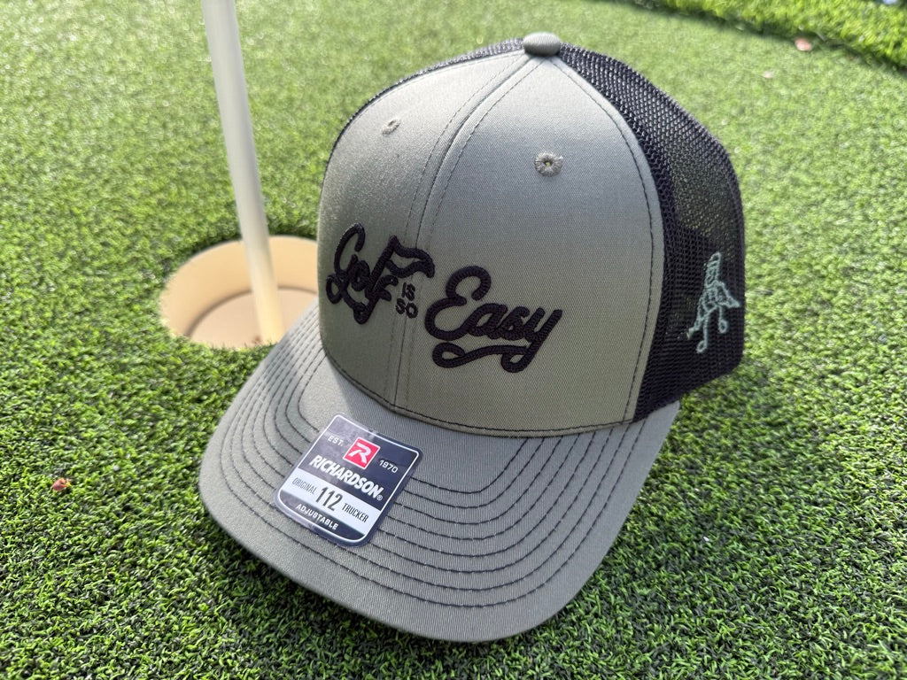 Gray and black cap with 'Golf is Easy' text on a golf course